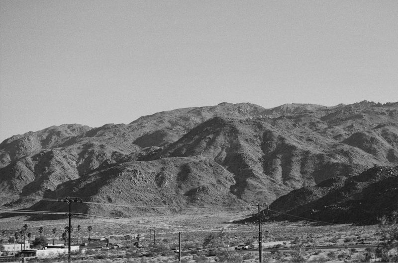 Monochromatic view of arid landscape with mountains, sky, and sparse vegetation, power lines traversing the scene.
