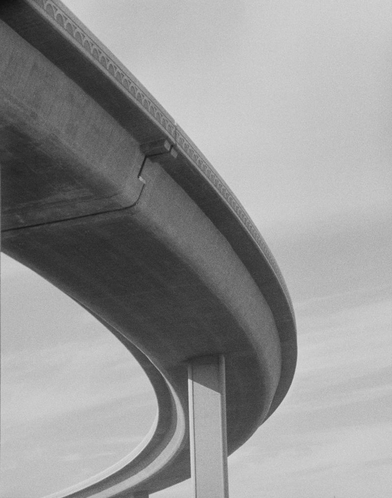 Low-angle monochrome shot of a concrete highway overpass with a curved design against a cloudy sky, emphasizing architectural lines.