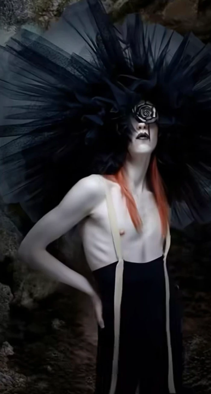 Model with dramatic black tulle headpiece and long red hair wearing dark trousers with suspenders in a natural rocky setting