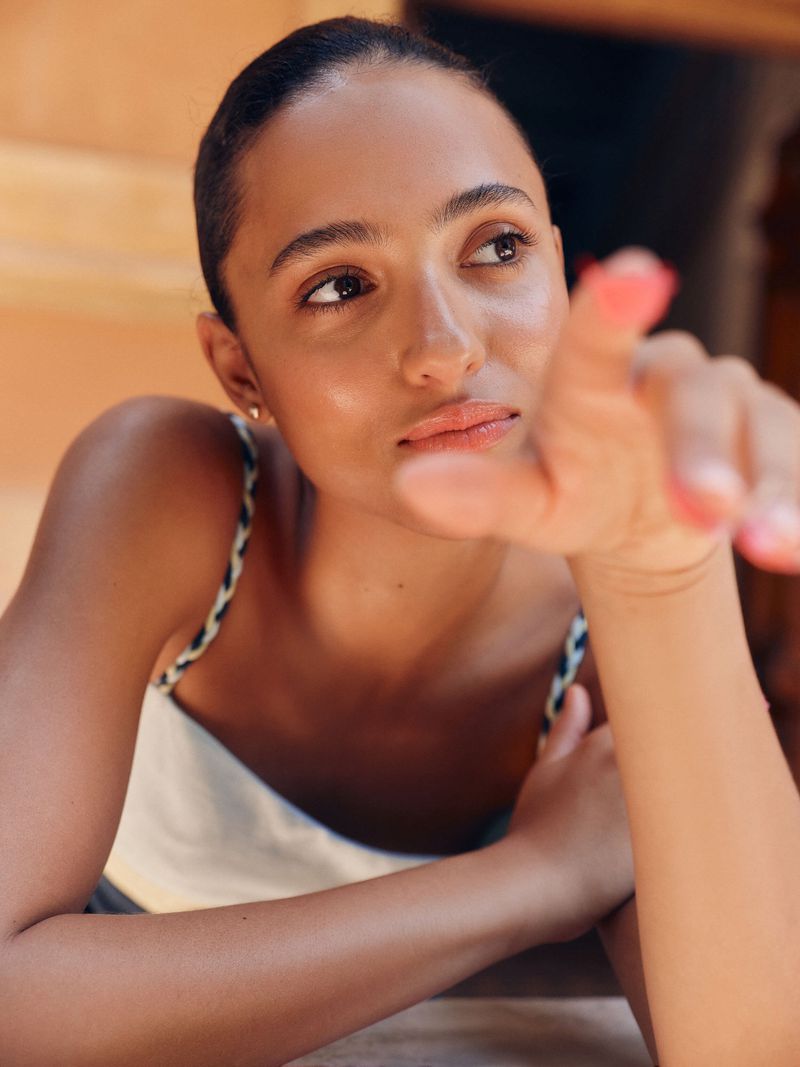 Portrait of an adult woman with tan skin, looking toward her extended hand in an indoor setting with soft, diffused natural lighting.