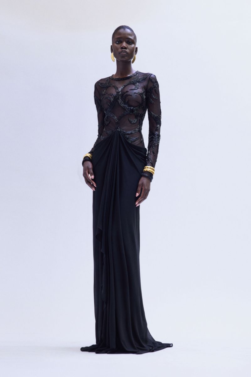 Elegant Black Woman in Gown: Full shot of a single adult female wearing a long black gown with sheer lacy sleeves and gold bracelets.