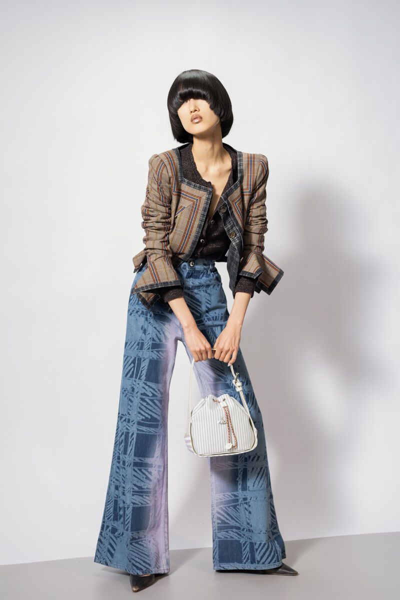Stylish woman poses in a plaid jacket and wide-leg jeans, holding a bucket bag against a white backdrop, fashion-forward and chic.