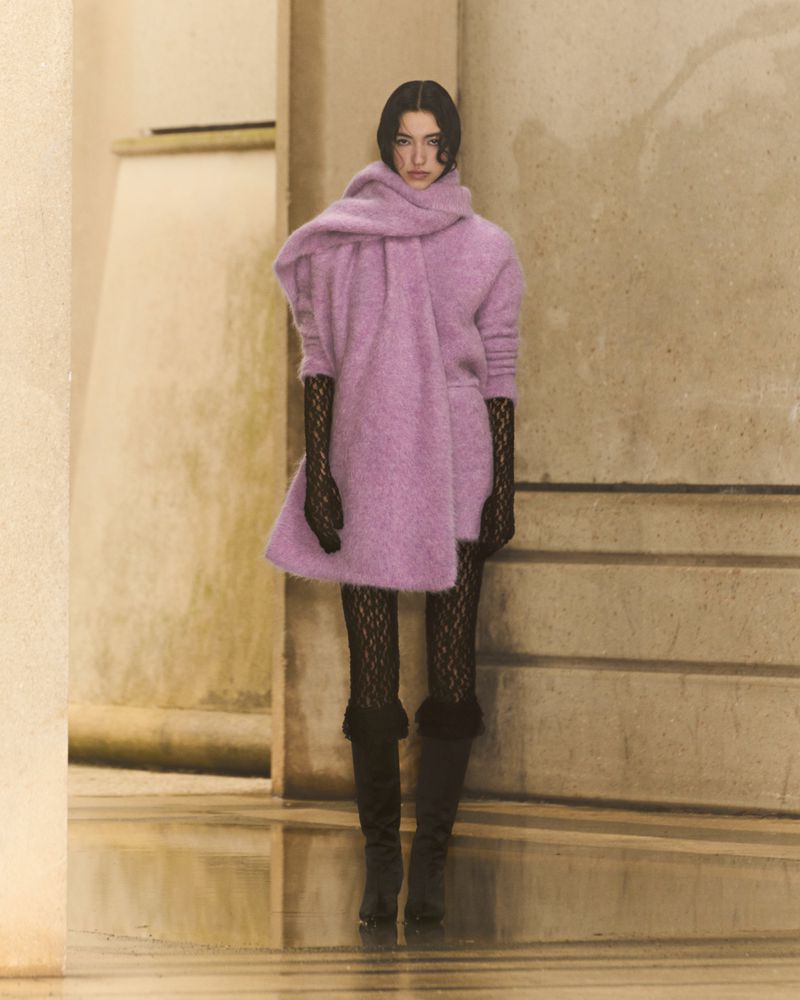 Elegant woman showcasing lavender knit dress with oversized scarf, black lace gloves, and dark knee-high boots in neutral-toned indoor space.