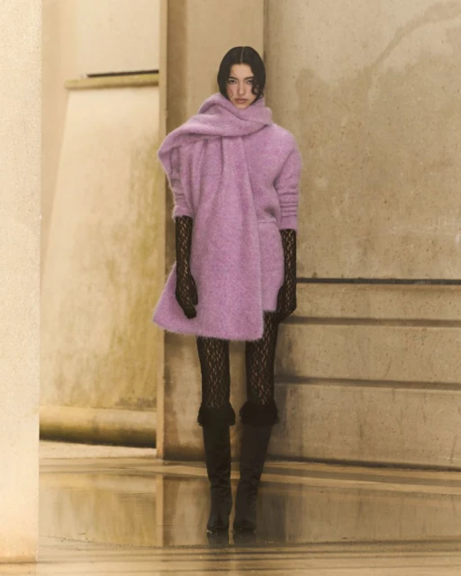 Elegant woman showcasing lavender knit dress with oversized scarf, black lace gloves, and dark knee-high boots in neutral-toned indoor space.