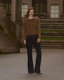 Red-haired female model wearing a textured brown sweater and dark flare trousers outdoors by classical stone steps
