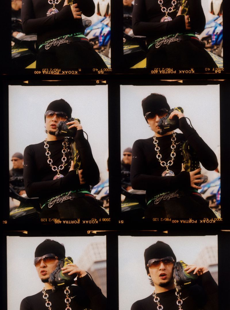 Man in sunglasses and beanie poses with shoe as phone against film strip of identical shots. Black long-sleeve shirt and large chain.