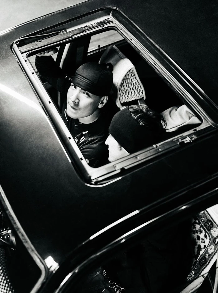 High-angle black and white shot of two people looking up through an open car sunroof