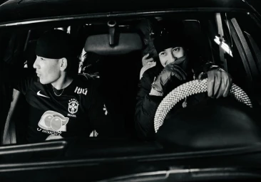 Monochrome image of two people inside a car at night, one holding the steering wheel and smiling.