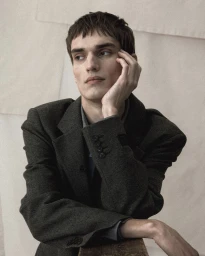 Close-up portrait of a man resting his chin on his hand, wearing a dark wool blazer against a neutral backdrop.