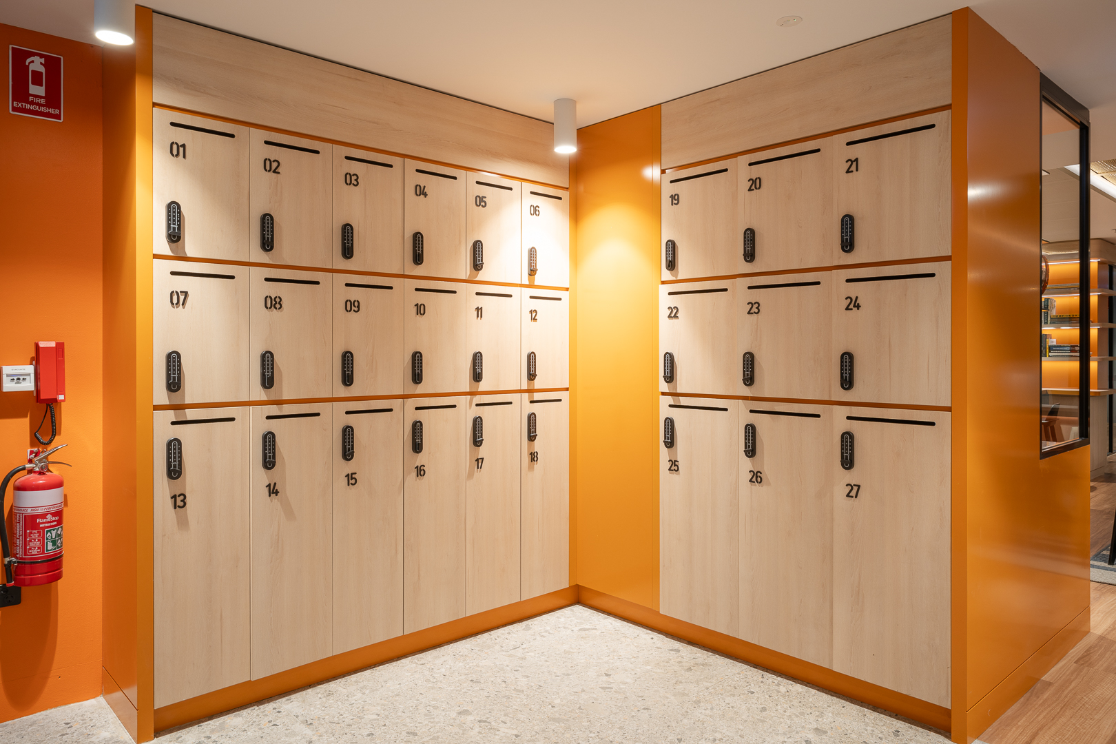Numbered lockers in light wood and orange line a hallway, providing a secure storage solution in a clean and organized environment.