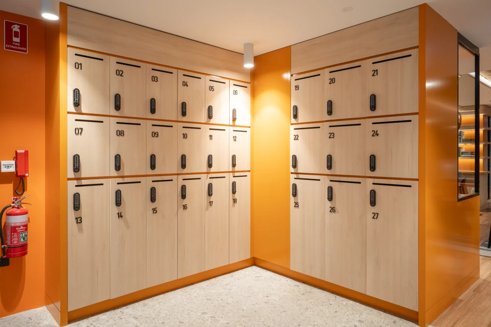 Numbered lockers in light wood and orange line a hallway, providing a secure storage solution in a clean and organized environment.