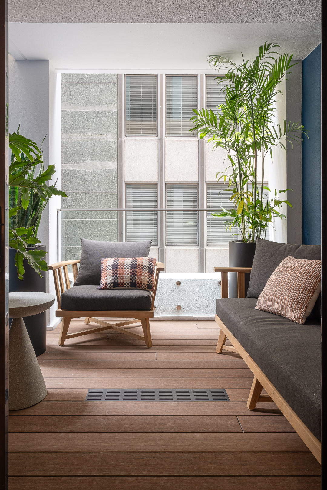Comfortable outdoor living space with cushioned armchairs, sofa, potted green plants, and a building exterior backdrop.