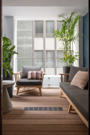 Comfortable outdoor living space with cushioned armchairs, sofa, potted green plants, and a building exterior backdrop.