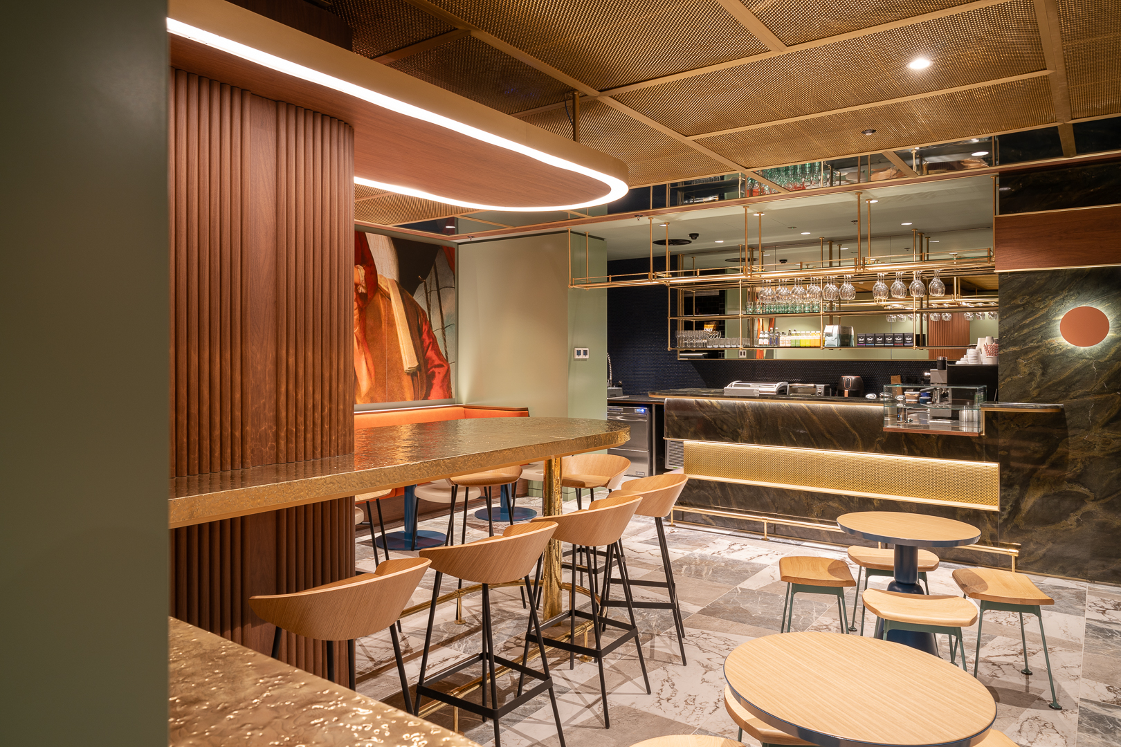 Interior of a modern cafe with warm lighting, featuring wooden chairs, tables, and a stylish bar with marble accents.