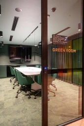 Interior view of a modern conference room named Green Room seen through a glass door with green rolling chairs and a long white table