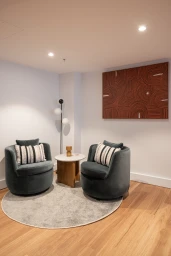 Two grey armchairs with striped pillows flank a small round table on a grey rug, with a large abstract artwork on the wall.