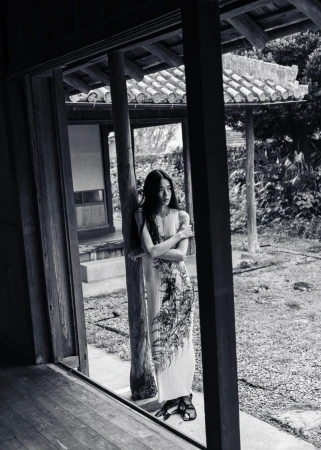 Monochrome full shot of a woman in a patterned dress standing in a traditional Japanese doorway looking toward the garden.