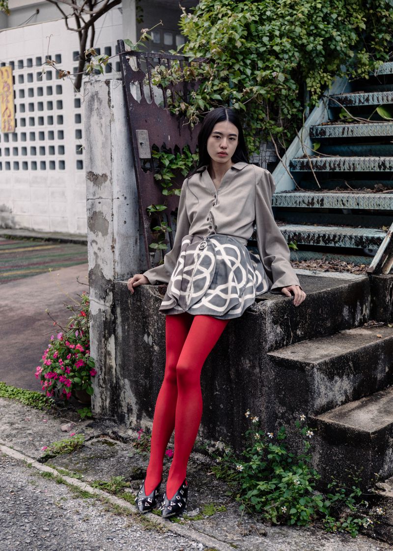A woman in a blouse and patterned skirt poses on concrete steps. She is wearing red tights and patterned flats in an outdoor setting.