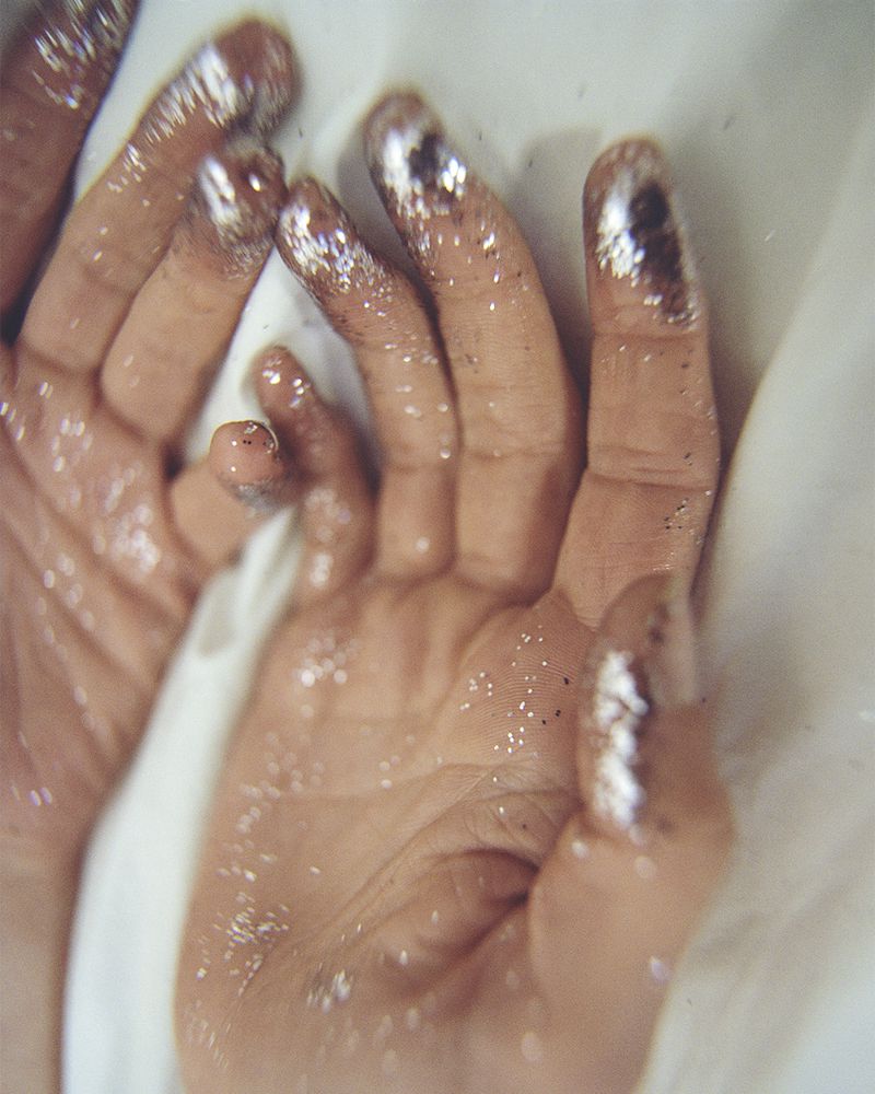 Close-up of two hands with glitter-dusted fingertips resting against white fabric