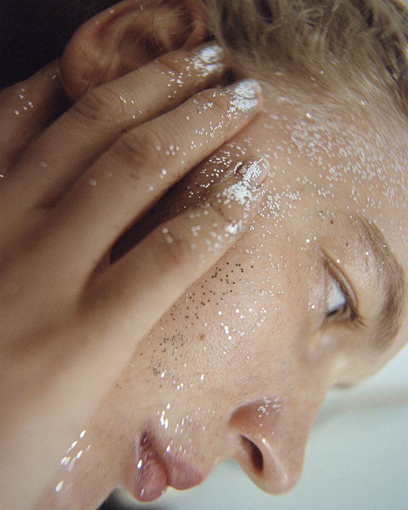 Close-up portrait of a woman's face partially covered with a hand and adorned with silver glitter makeup. Beauty shot.