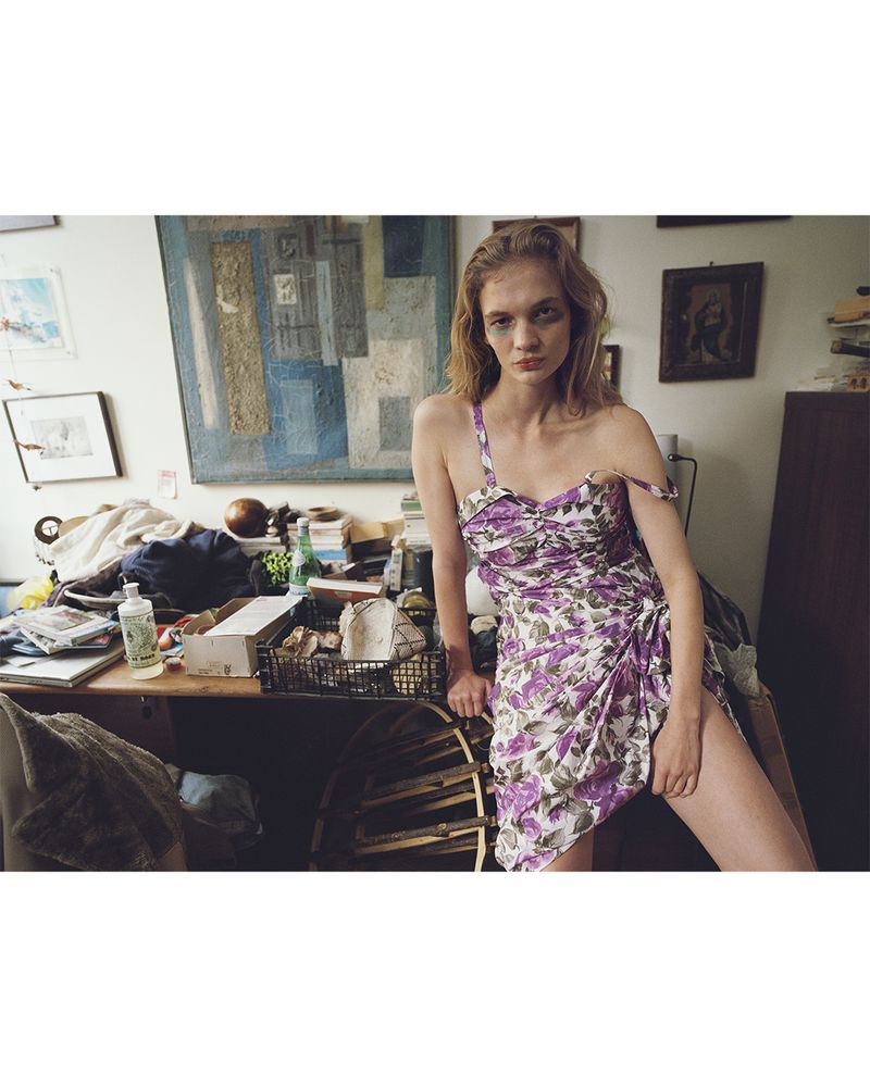 Model Caitlin Soetendal wearing a purple floral dress in a cluttered artist studio for D Repubblica.