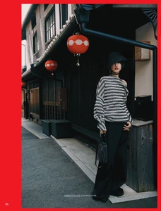 Model standing on a traditional street in Kyoto wearing a striped sweater, black hat, and holding a small handbag.
