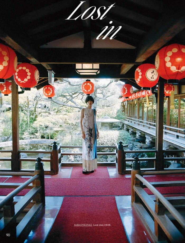 Model standing on a red carpeted wooden balcony framed by rows of bright red paper lanterns in a traditional Japanese setting.