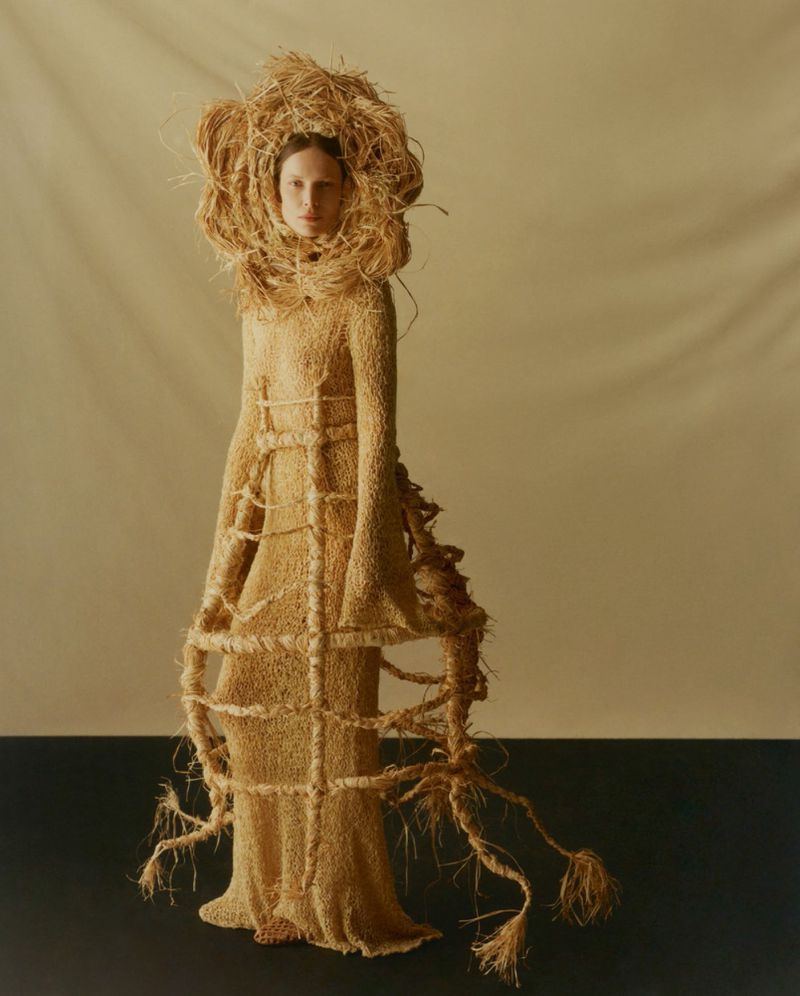 Model wearing a structured straw gown and sculptural headpiece against a neutral backdrop for Vogue Polska