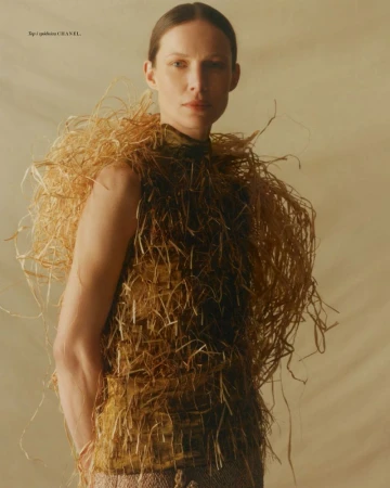 Model wearing a structured straw-textured garment standing against a neutral plain background for Vogue Polska
