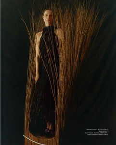 Model standing inside a sculptural vertical woven wicker structure against a dark background for Vogue Polska project Plecionka.