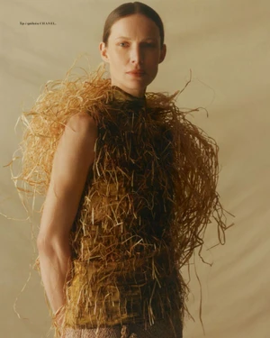 Model wearing a structured straw-textured garment standing against a neutral plain background for Vogue Polska