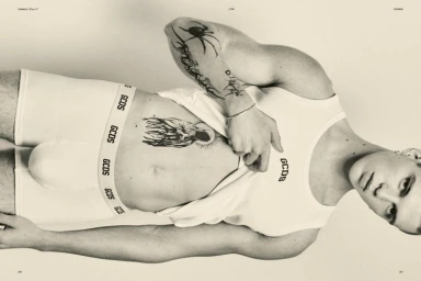 Close-up monochrome editorial portrait of a tattooed male model wearing white branded underwear and a tank top.