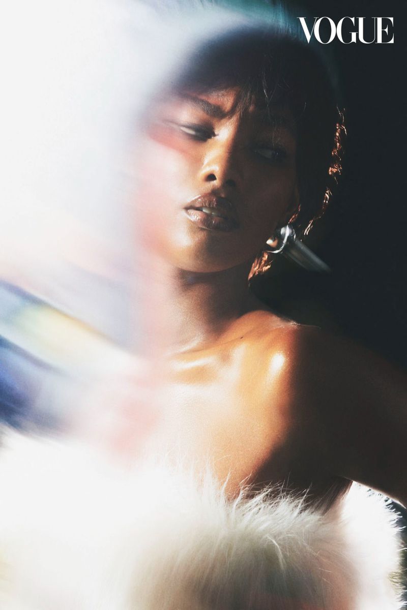 Portrait of a Black woman with short hair and shimmery makeup wearing statement earring, set against dark backdrop with Vogue logo.