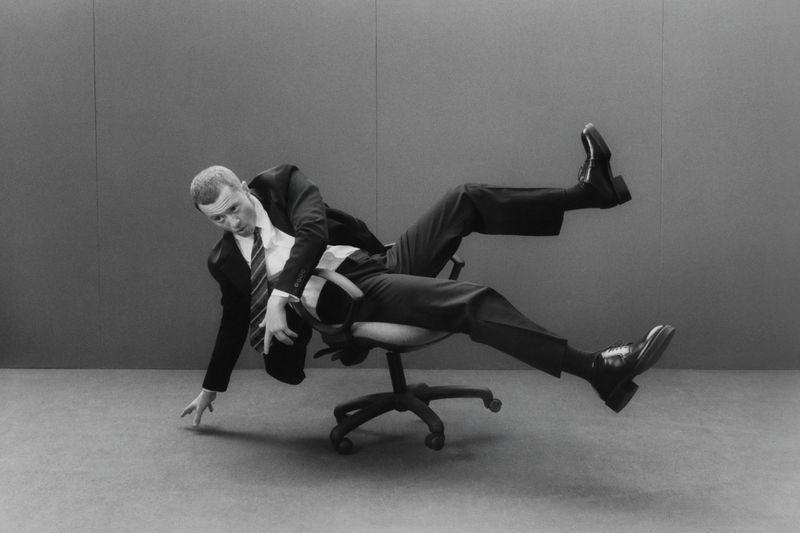 Monochrome portrait of a man in a suit falling backwards off an office chair, captured in a dynamic, humorous studio setting.