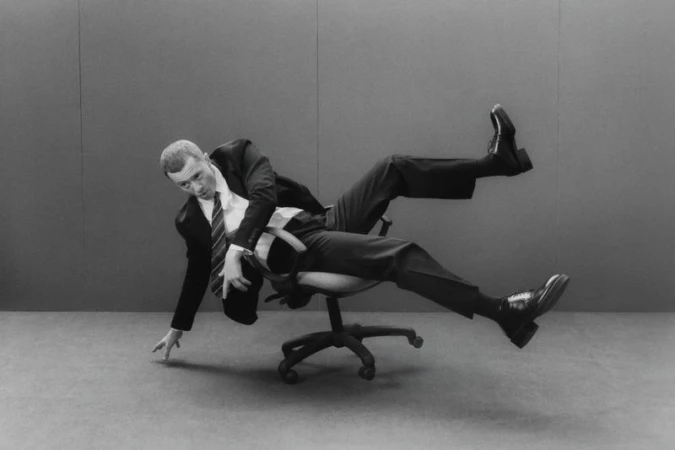 Monochrome portrait of a man in a suit falling backwards off an office chair, captured in a dynamic, humorous studio setting.