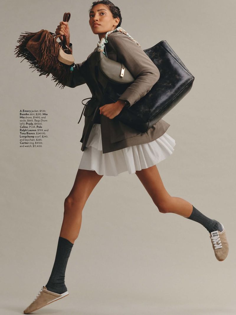 Fashion editorial shot of a woman in motion wearing a skirt, jacket and carrying handbags in a studio with neutral background.