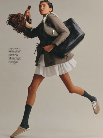 Fashion editorial shot of a woman in motion wearing a skirt, jacket and carrying handbags in a studio with neutral background.