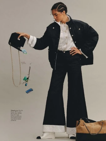 Fashion editorial shot of a biracial adult woman wearing a black Chanel jacket and flared pants, accessorized with jewelry and a handbag.
