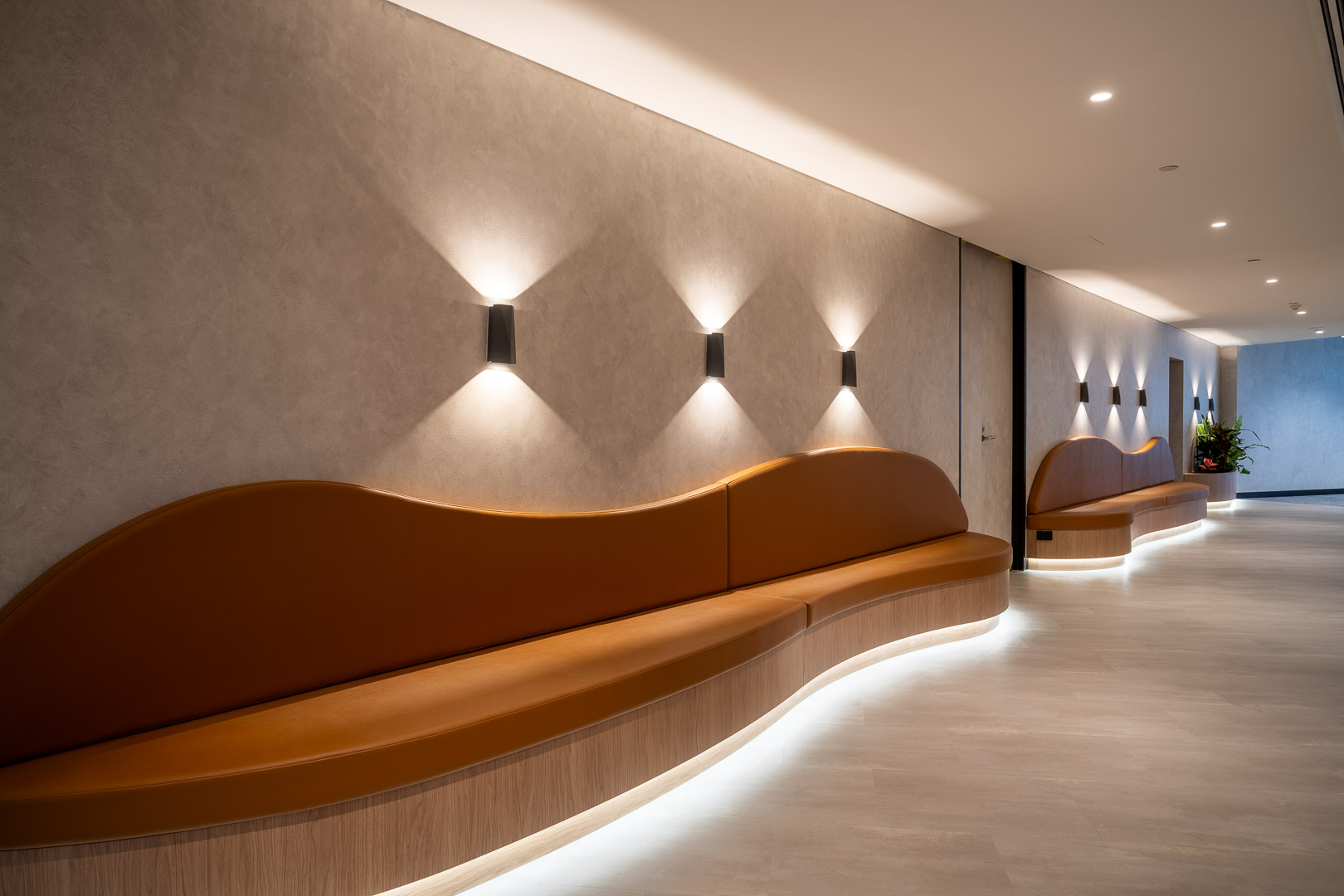 Contemporary interior design showcasing a curved bench with integrated lighting, set against a textured wall with sconce lighting fixtures.