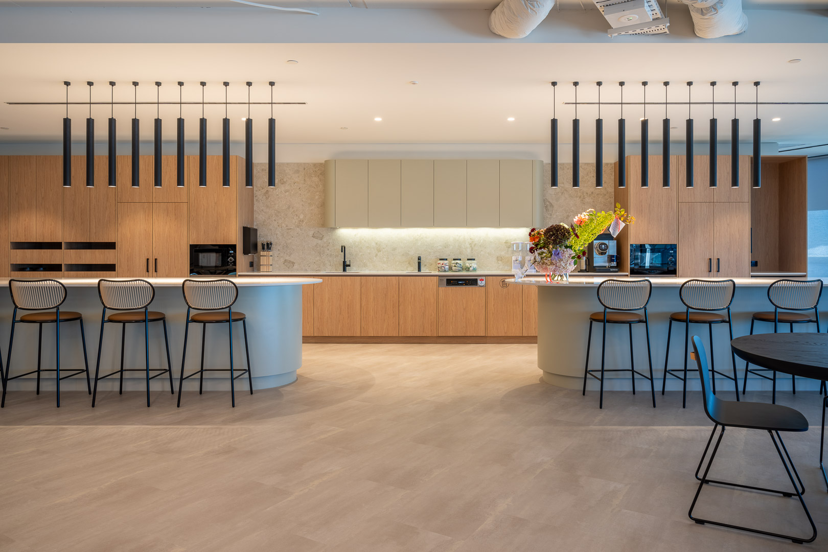 Modern office break room with sleek countertops, bar stools, contemporary lighting, and open design for employee relaxation and socializing.