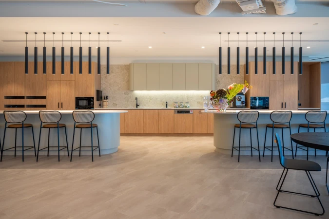 Modern office break room with sleek countertops, bar stools, contemporary lighting, and open design for employee relaxation and socializing.