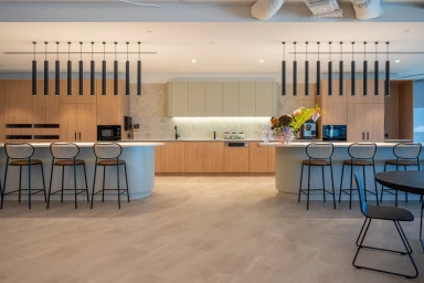 Modern commercial kitchen interior with light wood cabinetry, white curved islands, and black pendant lighting fixtures