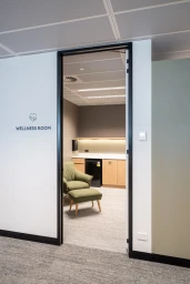 Interior shot of an office wellness room featuring an armchair with an ottoman viewed through an open doorway.