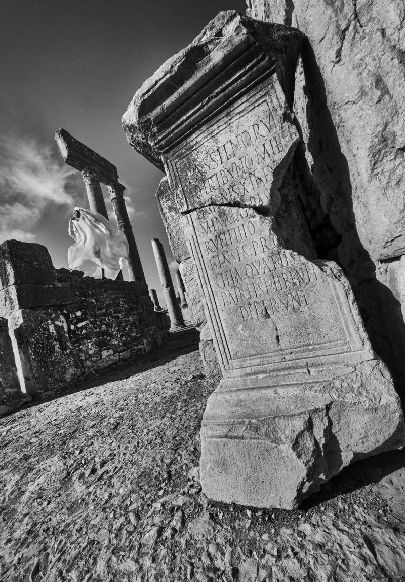 Monochrome image showcases ancient stone ruins, featuring weathered columns and an engraved stone block under a clear sky, architecture.
