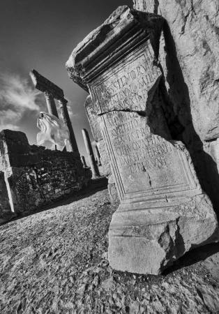 Monochrome image showcases ancient stone ruins, featuring weathered columns and an engraved stone block under a clear sky, architecture.