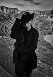 Man wearing a black coat and hat standing on the tiered stone seats of an ancient amphitheater