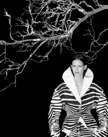 Black-and-white fashion portrait of an adult female in a zebra-print coat with a large white collar, standing under bare tree branches.