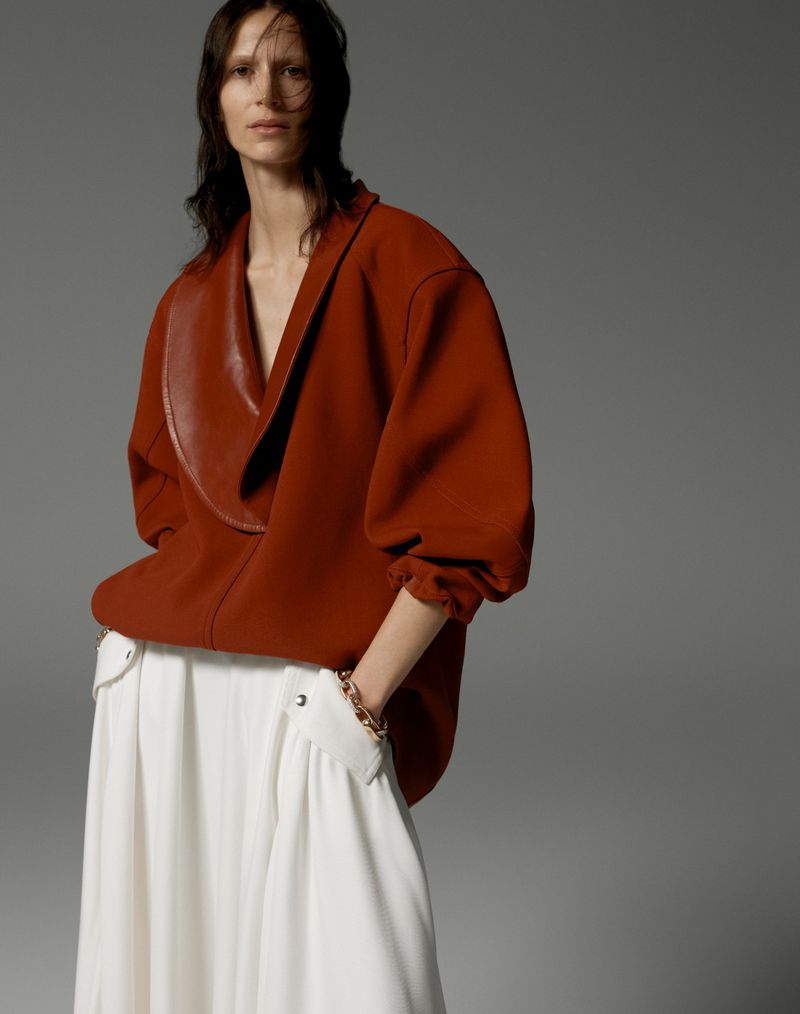 Woman in terracotta top and white skirt in a studio fashion shot. The neutral backdrop highlights the clothing and minimalist style.