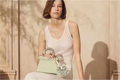 Model wearing a white ribbed dress holding a pale green handbag against a warm neutral wall with leaf shadow patterns.