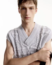 Portrait of a male model wearing a textured grey knit vest against a clean white background for Dior Men.